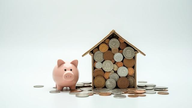 A small house made of coins and a piggy bank, representing building a secure emergency fund.